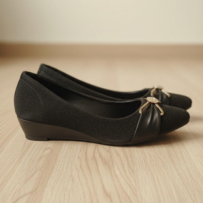 Pair of black shoes with a decorative bow on a wooden surface