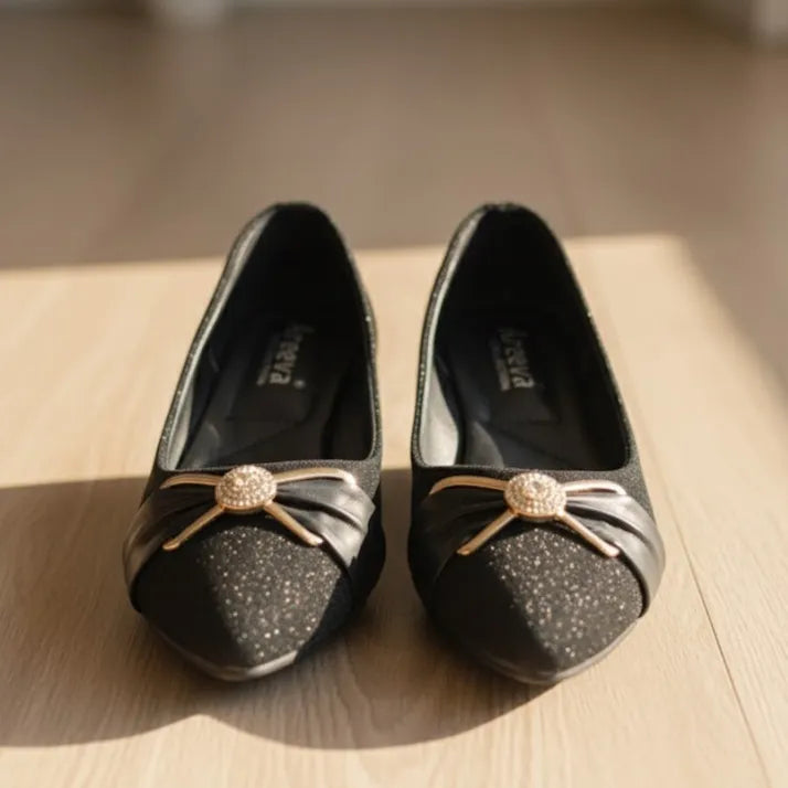 Pair of black shoes with decorative bows on a wooden surface