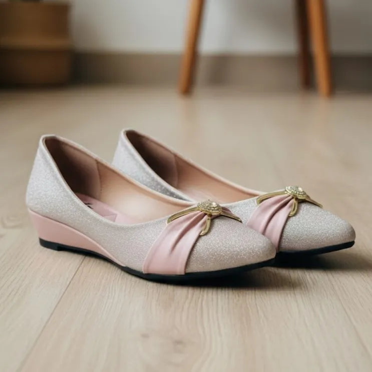 Pair of pink shoes with pink bow and gold accents on a wooden floor.