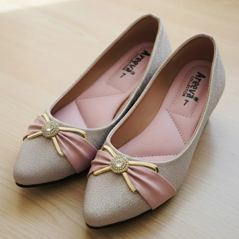 Pair of glittery shoes with pink bows and decorative elements on a light wooden surface.