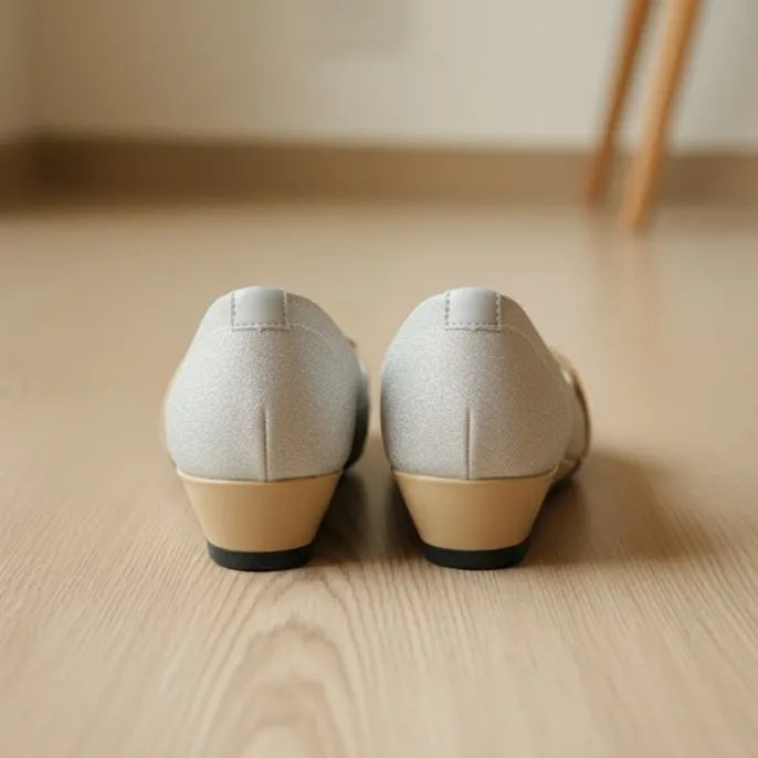 Pair of light gray shoes with beige soles on a wooden floor.