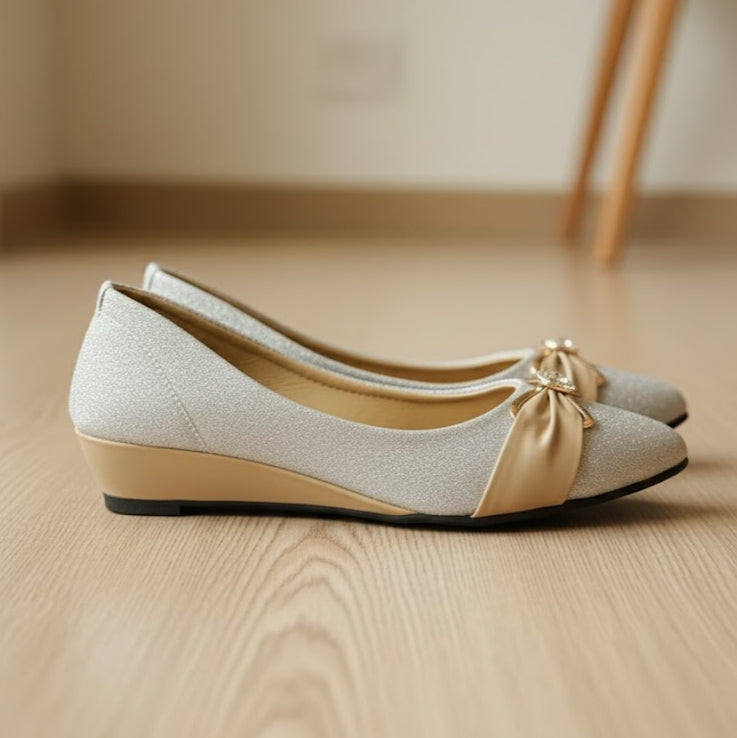Pair of light gray shoes with a gold bow on a wooden floor.