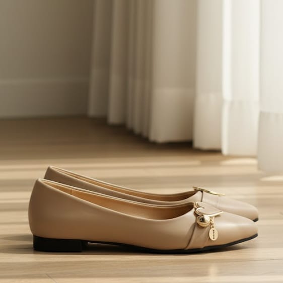 Pair of beige flat shoes with a decorative bow on a wooden floor.
