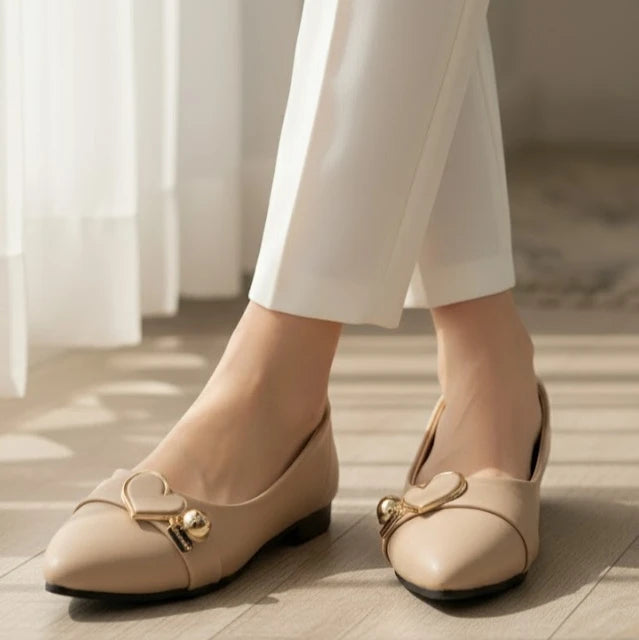 Beige shoes with gold accents worn by a person in white pants on a wooden floor.
