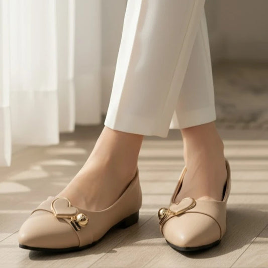 Beige shoes with gold accents worn by a person in white pants on a wooden floor.