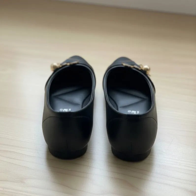 Pair of black shoes with gold accents on a light wooden surface