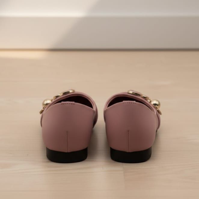 Pair of pink loafers with gold accents on a light wooden floor.