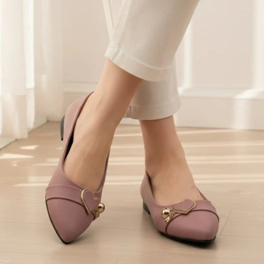 Pink shoes with gold accents worn by a person on a light wooden floor.