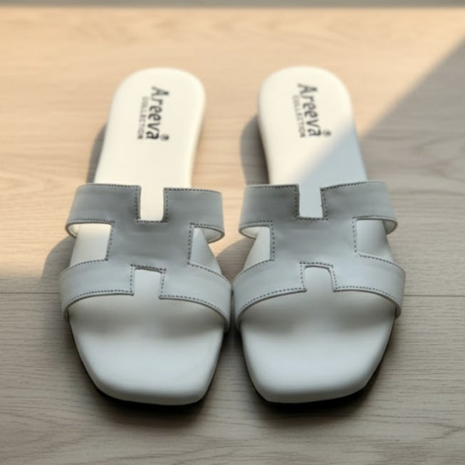 Pair of white sandals with 'Areeva branding on a wooden surface