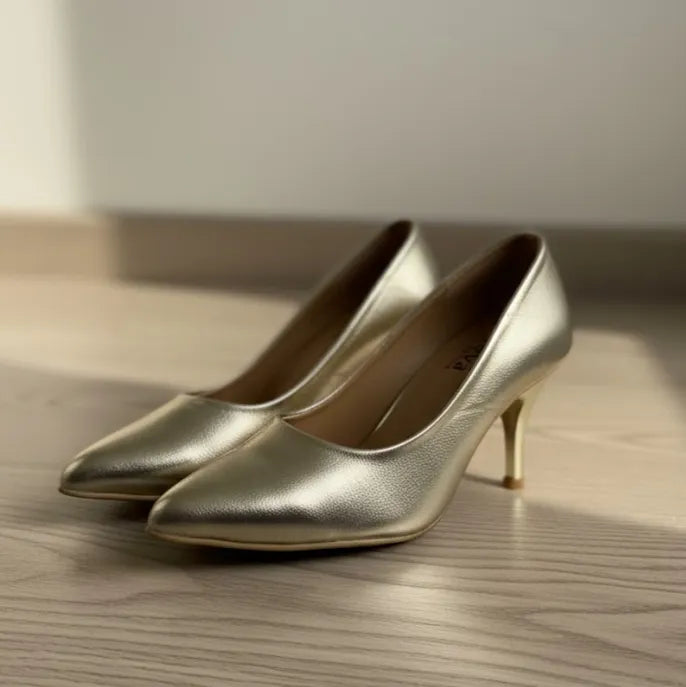 Pair of gold high-heeled shoes on a wooden surface with a neutral background