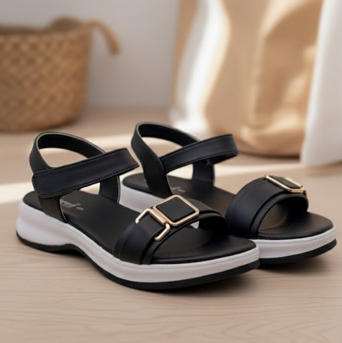 Black sandals with gold buckles on a wooden surface
