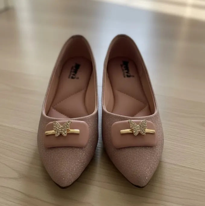 Pair of pink shoes with gold butterfly decorations on a wooden surface