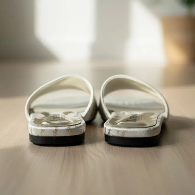 Pair of white slippers with black soles on a wooden floor.